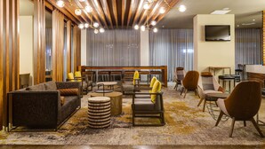 Eine moderne Hotelhalle mit einer Couch, Sesseln, einem Fernseher und einem gemusterten Teppich.