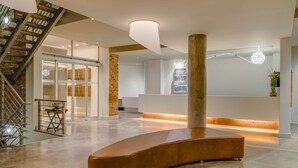 Eine geräumige Lobby mit einer geschwungenen Sitzecke, einer Treppe und einer Rezeption.