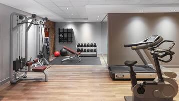 Ein Fitnessraum mit Trainingsgeräten, Laufband und Wandregal für Kurzhanteln.