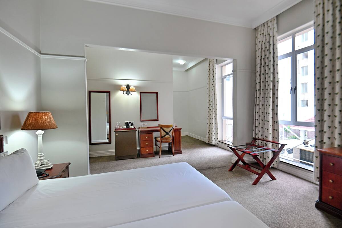 A hotel room with a bed, desk, chair, and a window with curtains.