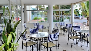 A covered outdoor seating area with striped chairs and tables, large windows, and potted plants. - The Balmoral Hotel (Durban)
