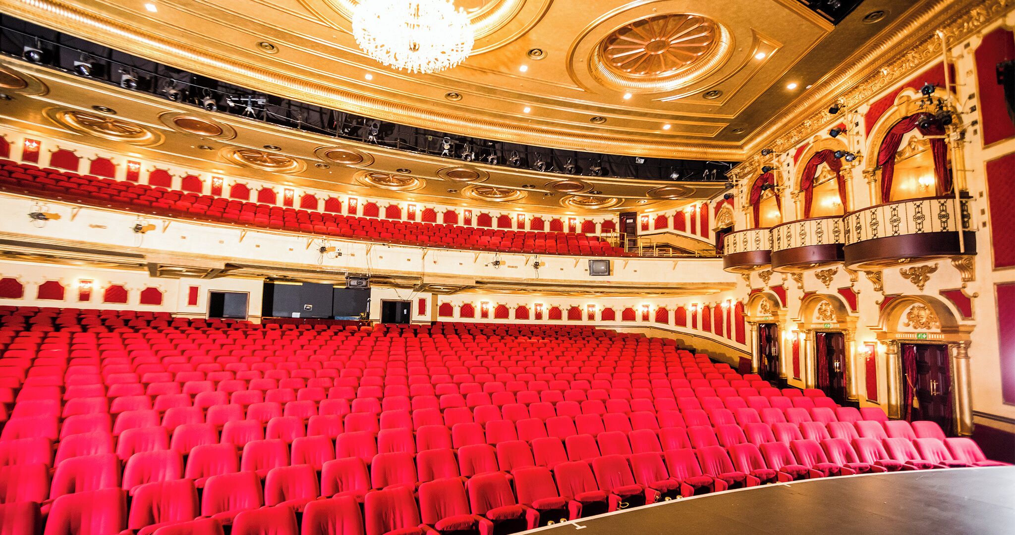 Um teatro grande e ricamente decorado, com assentos vermelhos e um imponente candelabro.