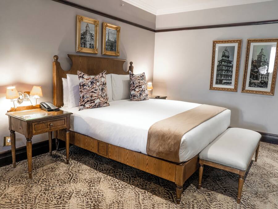 A hotel room with a large bed, wooden headboard, two bedside tables with lamps, a bedside phone, and a patterned carpet.