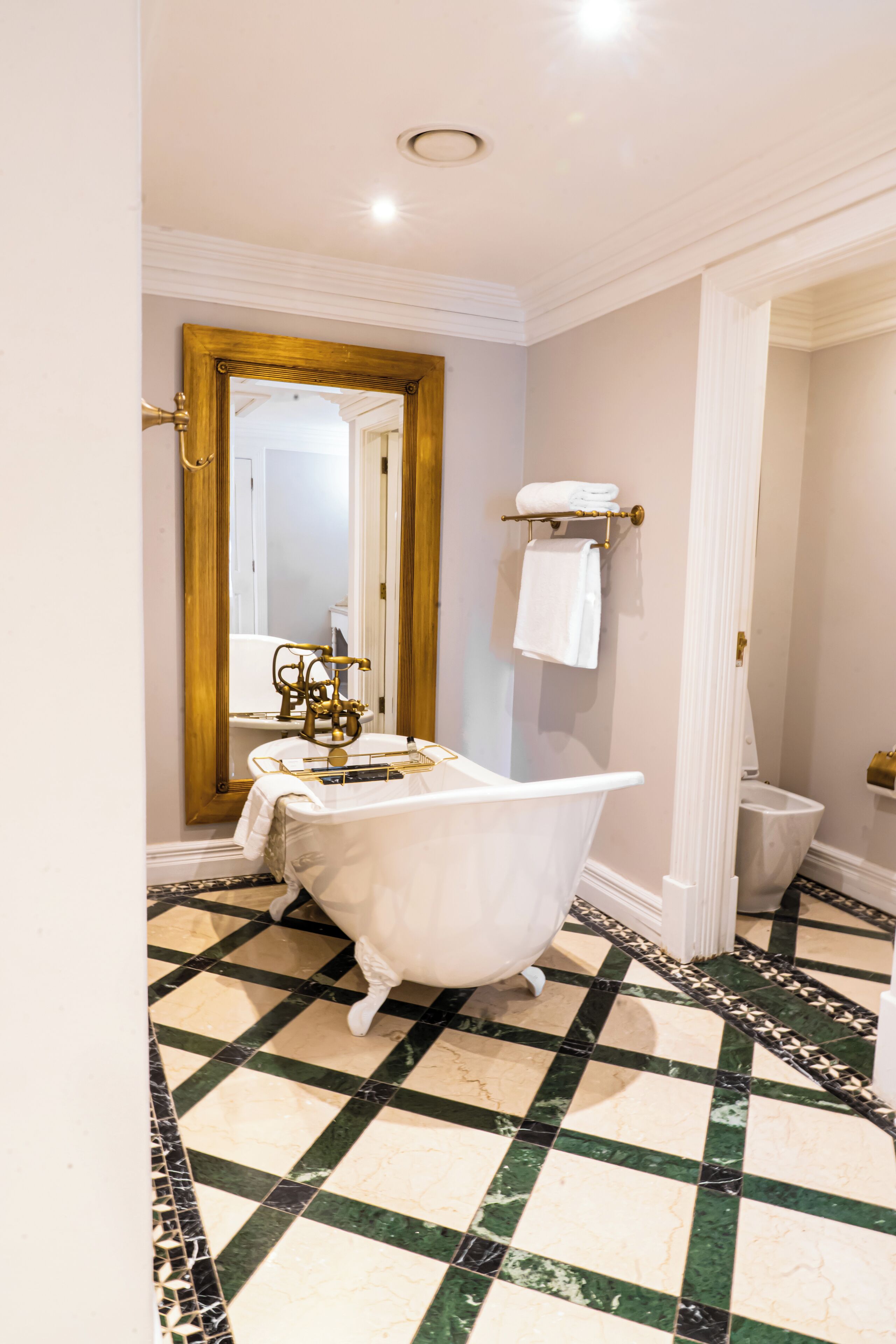 A bathroom with a clawfoot bathtub, a gold-framed mirror, and a checkered floor.