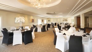 Un amplio salón de banquetes con varias mesas redondas dispuestas para comer, elegantes candelabros y suelo alfombrado.