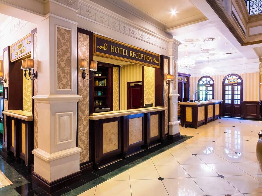 Zona de recepción de hotel con mostrador, caja registradora y un cartel que dice "HOTEL RECEPTION".