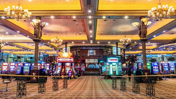 Un casino con numerosas máquinas tragamonedas, candelabros y un letrero que dice 'Pavilion Cafe'.