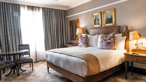 Habitación de hotel con una cama grande, dos mesitas de noche, un escritorio con una silla y una alfombra estampada.
