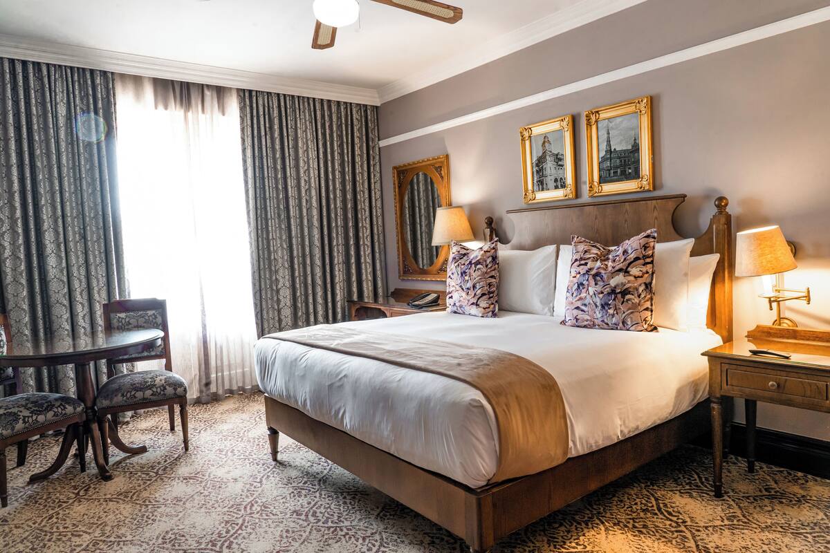 A hotel room with a large bed, two bedside tables, a desk with a chair, and a patterned carpet.
