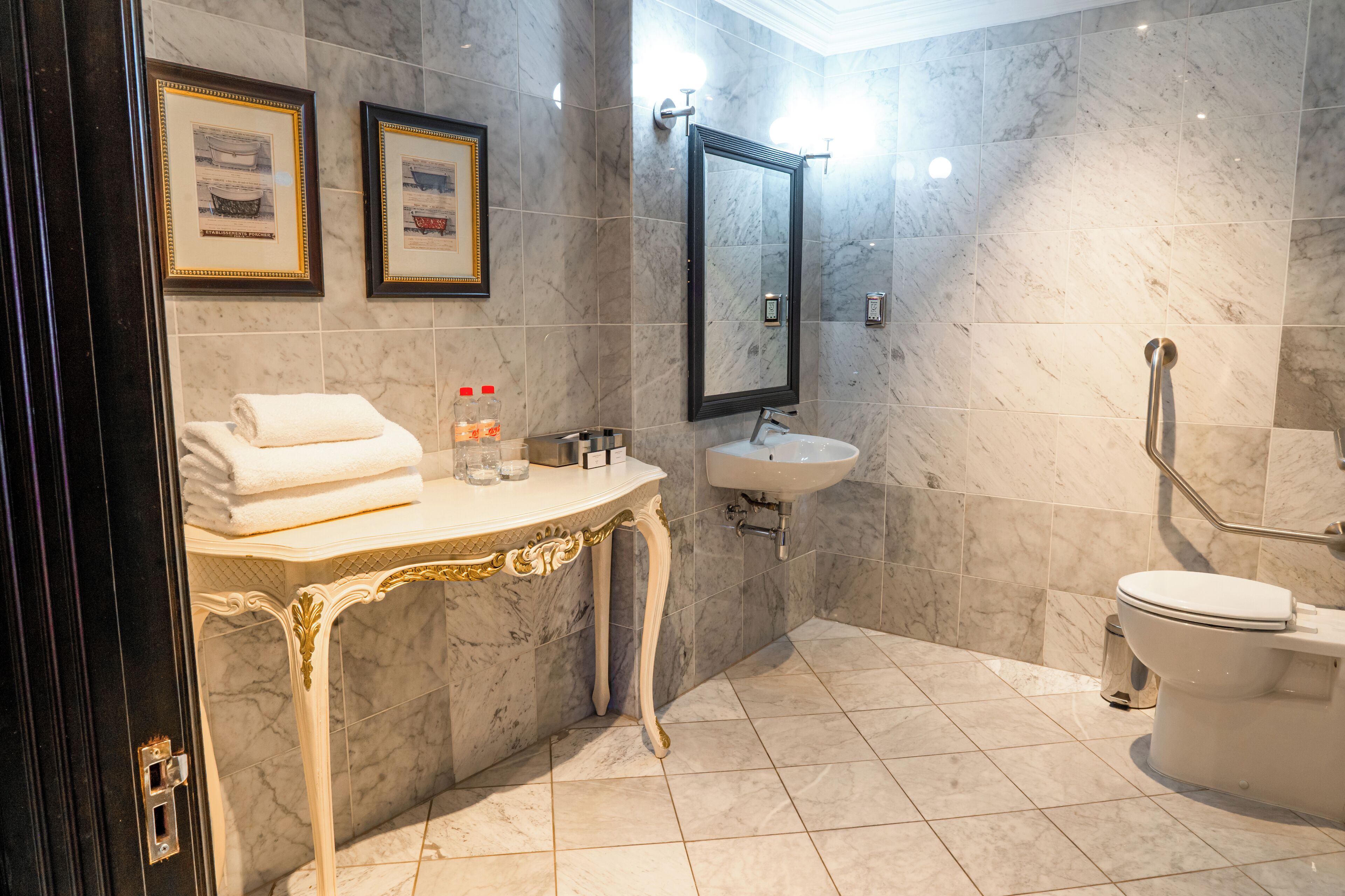 Un baño con paredes de mármol, un lavamanos, un inodoro y un mueble de tocador con toallas y artículos de aseo.