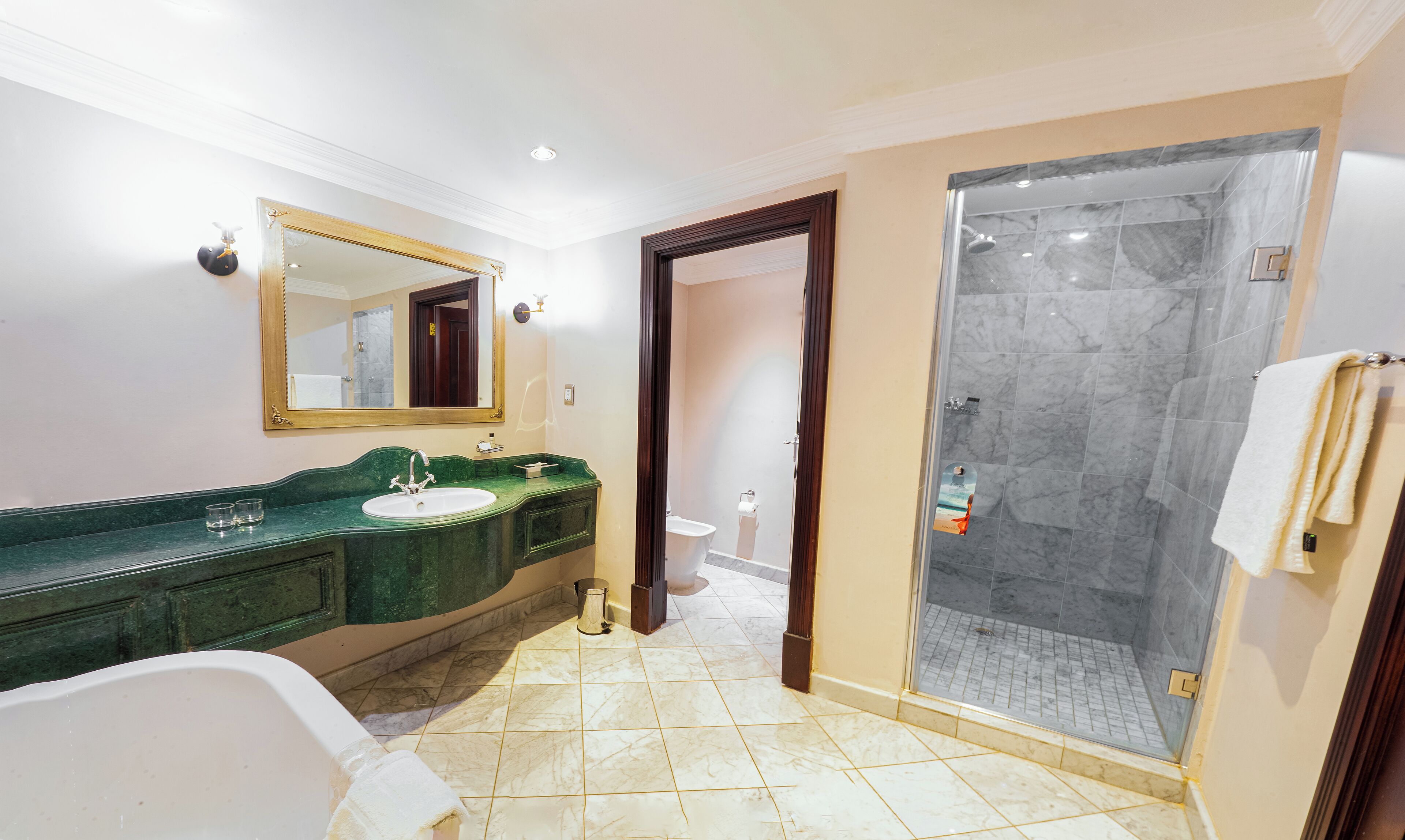 Une salle de bain avec un lavabo en marbre, une baignoire, un grand miroir et une douche à parois de verre.