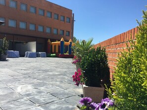 Un patio con pared de ladrillo, suelo de baldosas y una estructura inflable de colores para jugar.