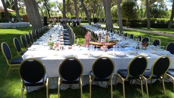 A long outdoor dining table set with chairs, a decorative boat centerpiece, and a well-maintained lawn.