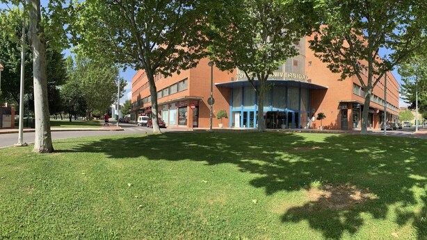A building with a sign reading 'Universidad' and a grassy area in front.