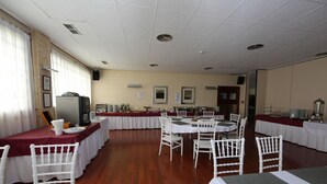 A banquet hall with multiple round tables, white chairs, and a long buffet table. - Universidad (Albacete)