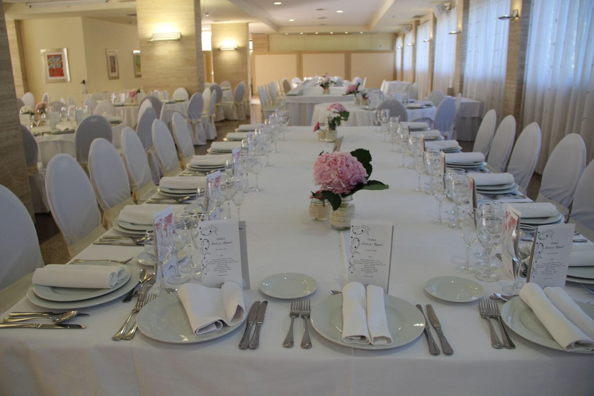 A banquet hall with tables set for a formal event, featuring white tablecloths, neatly arranged place settings, and floral centerpieces.
