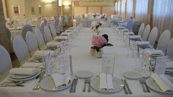 A banquet hall with tables set for a formal event, featuring white tablecloths, neatly arranged place settings, and floral centerpieces.
