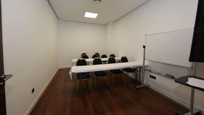 Een vergaderruimte met een witte tafel, zwarte stoelen, een whiteboard en een projectiescherm.