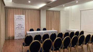 A conference room with a long table, rows of chairs, and a banner with hotel information.