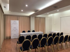 Un salón de conferencias con una larga mesa, filas de sillas y un cartel con información del hotel.