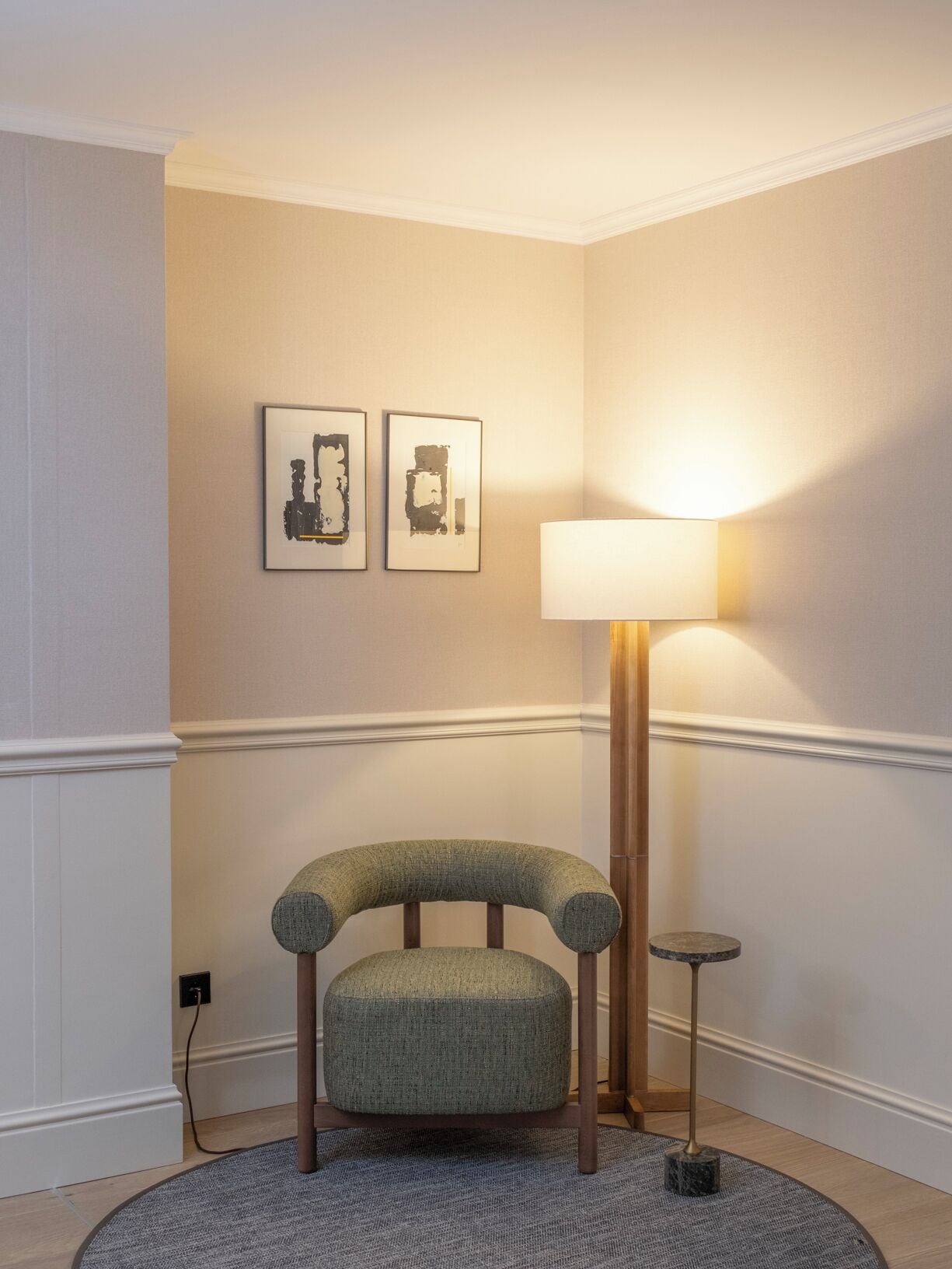Ein Eckzimmer mit einem grünen Sitzmöbel, einer Stehlampe und zwei gerahmten Kunstwerken an der Wand.