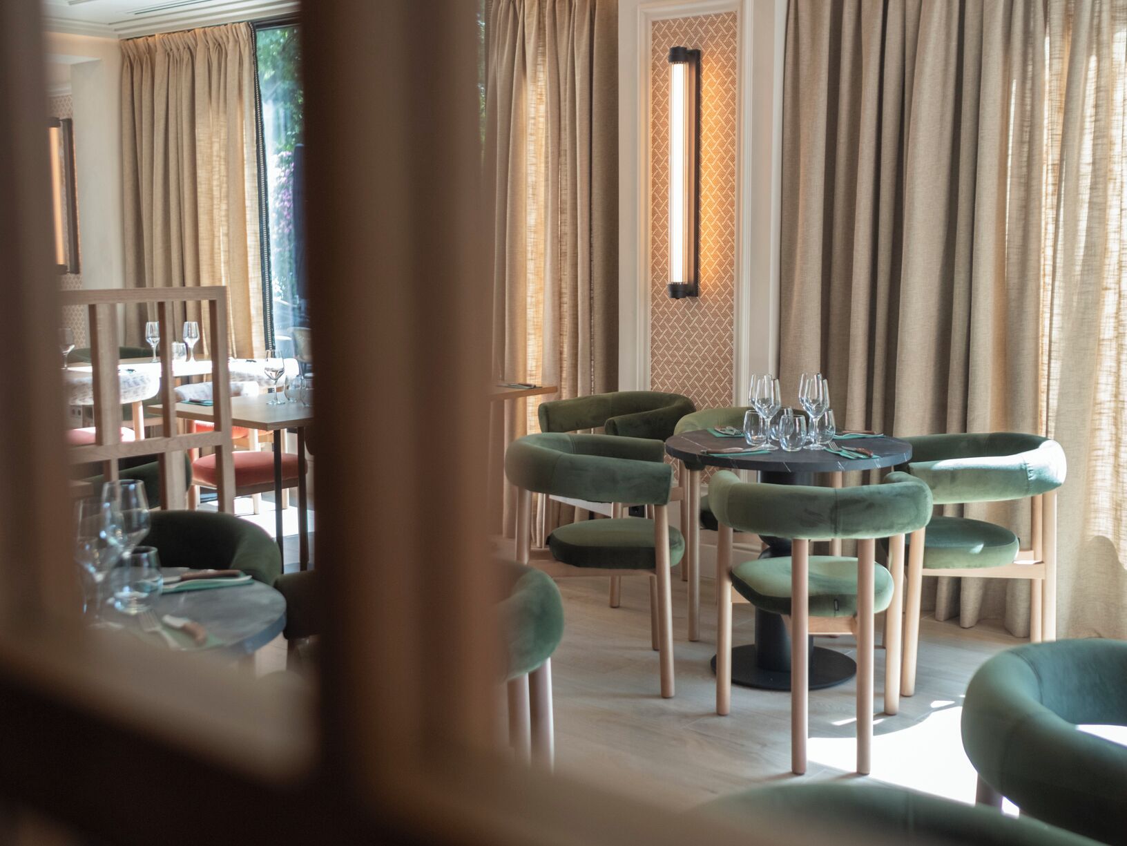 A restaurant interior with round tables, green upholstered chairs, and a patterned wall.