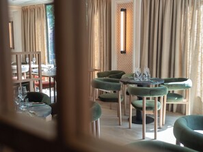 A restaurant interior with round tables, green upholstered chairs, and a patterned wall. - Hotel Cisneros (Alcala de Henares)