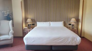 Een hotelkamer met een groot bed, twee nachtkastjes met lampen, een stoel en een decoratief wandpaneel.