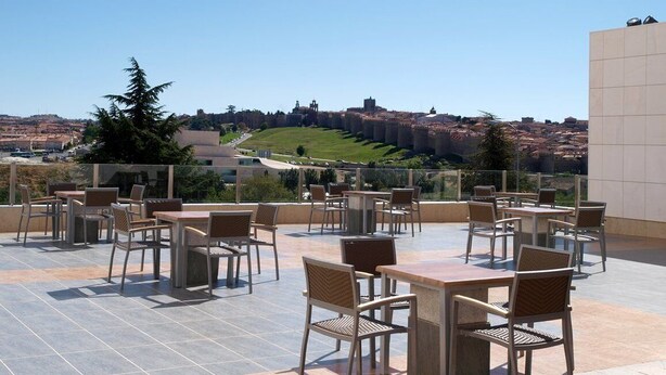 Terraço no telhado com área de estar externa, vista clara da paisagem urbana e um prédio grande ao fundo.