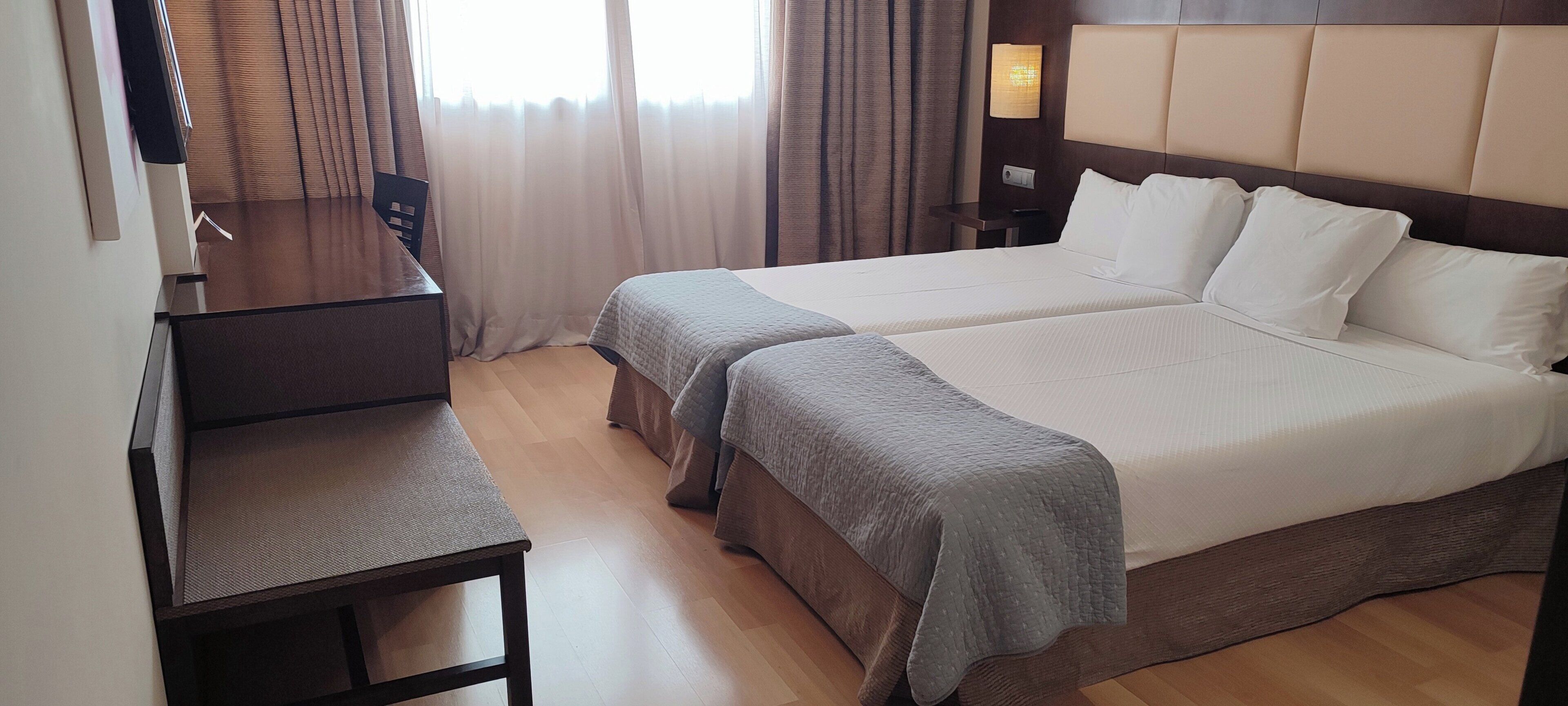 A hotel room with two beds, a desk, and a chair.