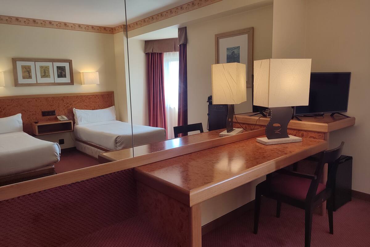 A hotel room with two beds, a desk with a chair, a television, and a mirror.