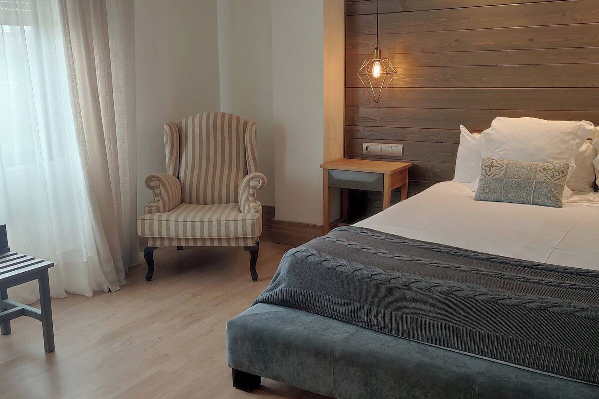 A bedroom with a bed, a chair, a bench, and a nightstand.