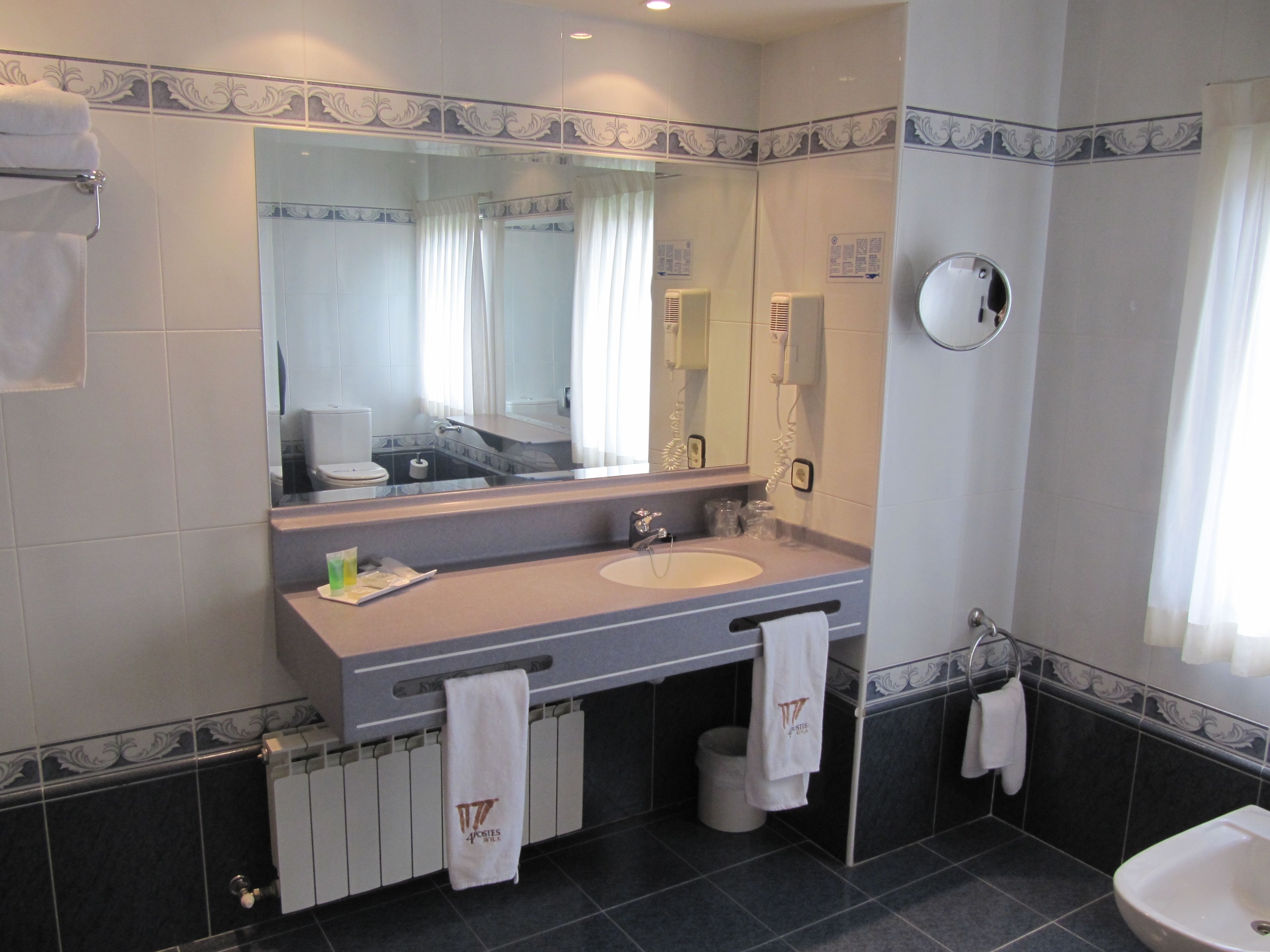 Une salle de bain avec un grand miroir, deux lavabos, des toilettes et une douche.