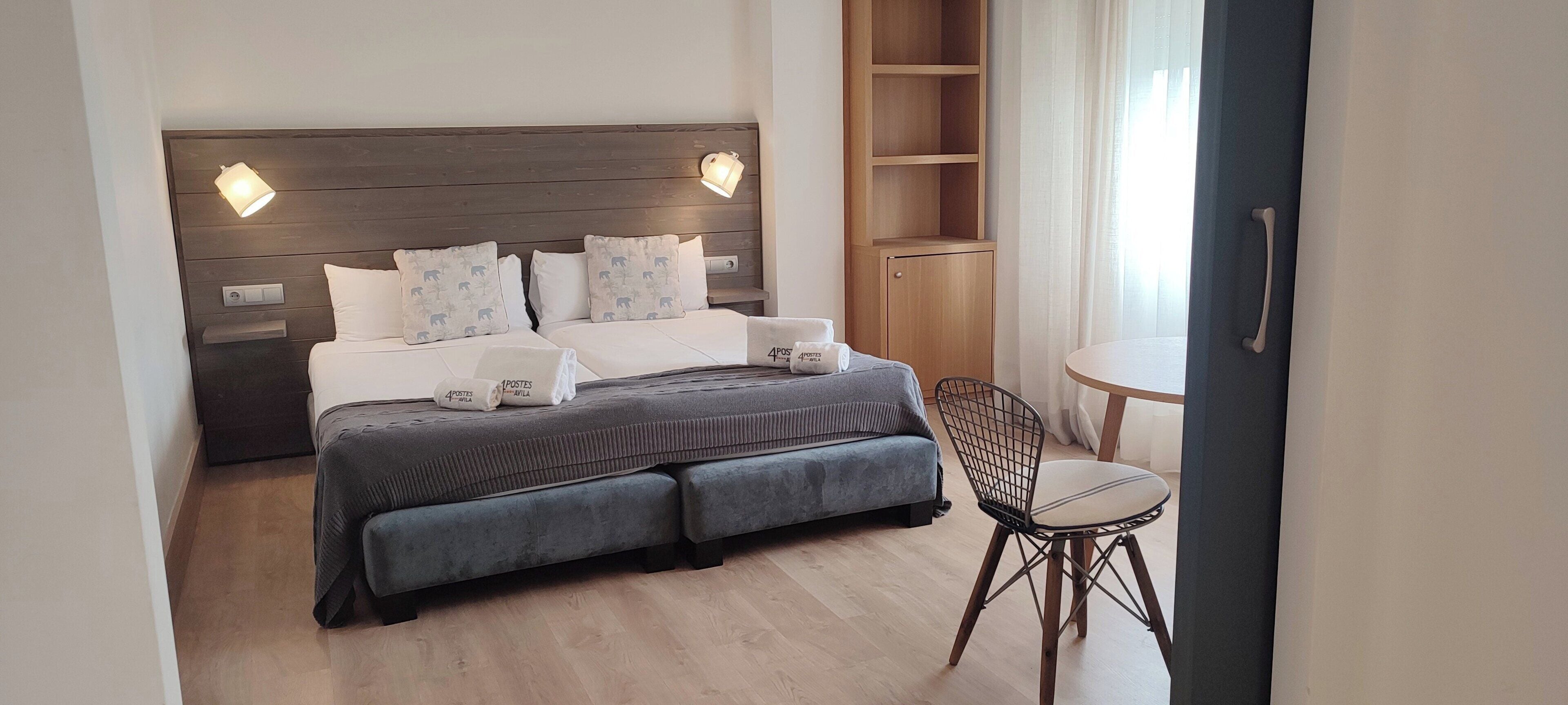 Una habitación de hotel con una cama grande, lámparas de noche, una mesita con una silla y un armario.