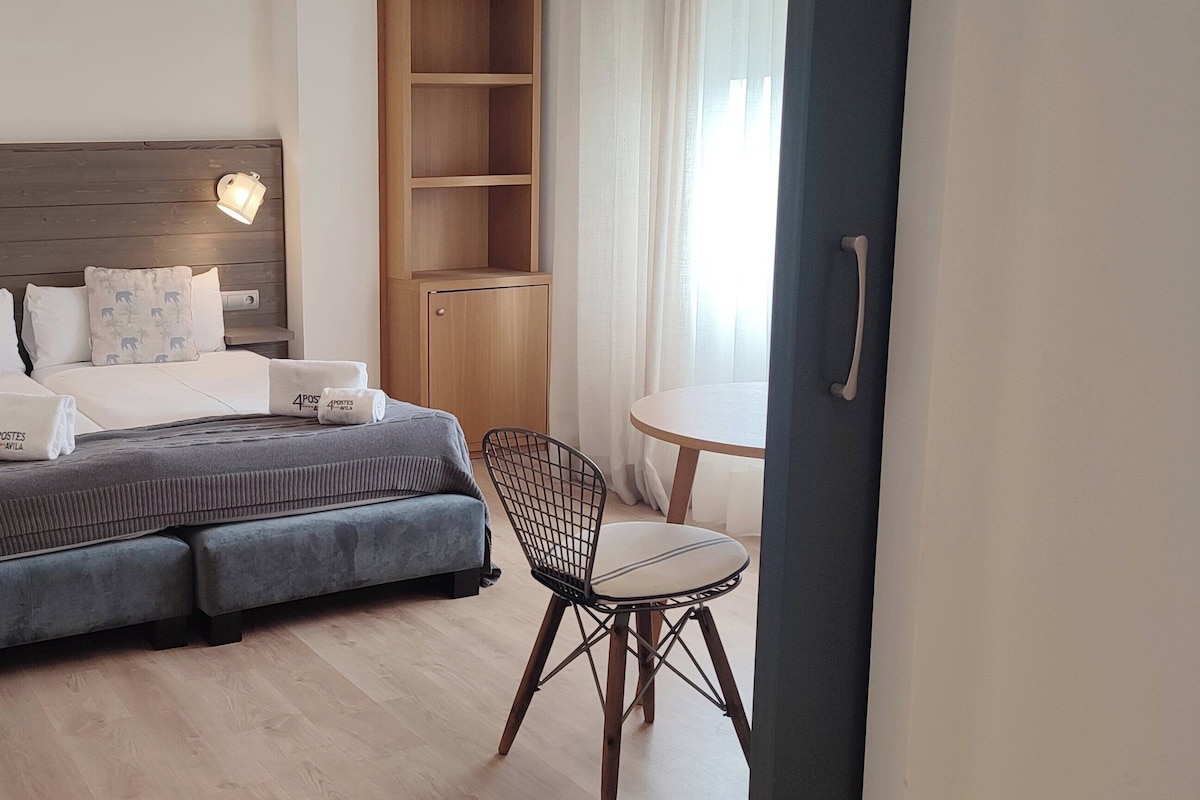 Una habitación de hotel con una cama grande, lámparas de noche, una mesita con una silla y un armario.