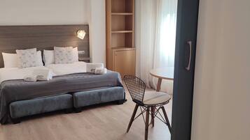 Una habitación de hotel con una cama grande, lámparas de noche, una mesita con una silla y un armario.