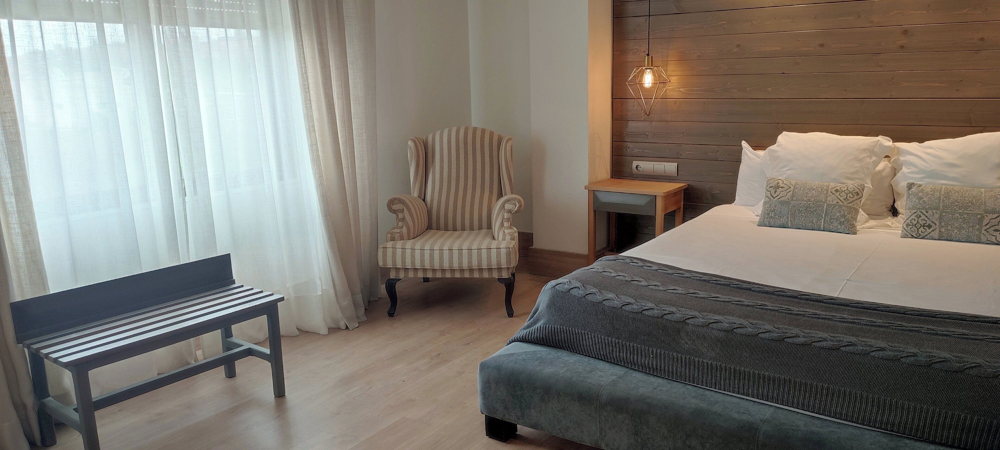 Un dormitorio con cama, una silla, un banco y una mesita de noche.