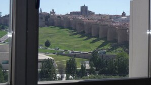 A view of a historic castle with a large wall and a tower, surrounded by green fields and a road with vehicles. - Hotel Sercotel Cuatro Postes (Ávila)