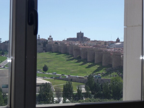 A view of a historic castle with a large wall and a tower, surrounded by green fields and a road with vehicles. - Hotel Sercotel Cuatro Postes (Ávila)