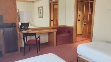 Habitación de hotel con cama, escritorio con silla, refrigerador pequeño y puerta que da a otra habitación.