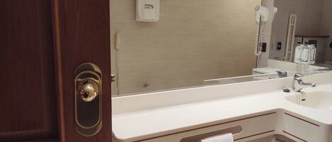 A hotel bathroom with a large mirror, a white sink, a hairdryer, and a towel rack.