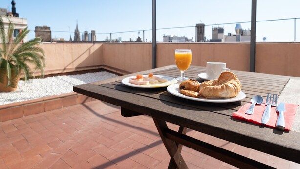 A rooftop terrace with a table set for breakfast, including croissants, a glass of orange juice, and a cup. - Hotel Turin  Barcelona  (Barcelona)