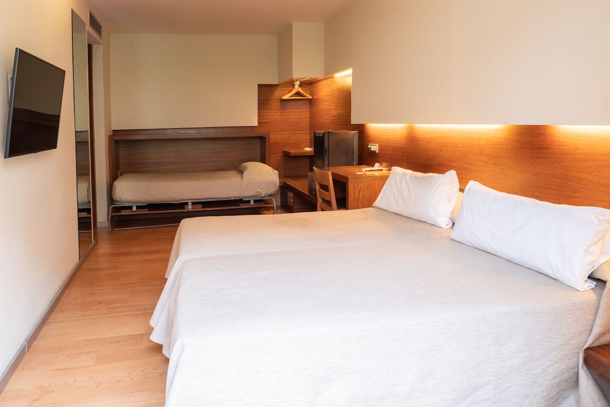 A hotel room with a large bed, a desk, a chair, a TV, and a wooden headboard.