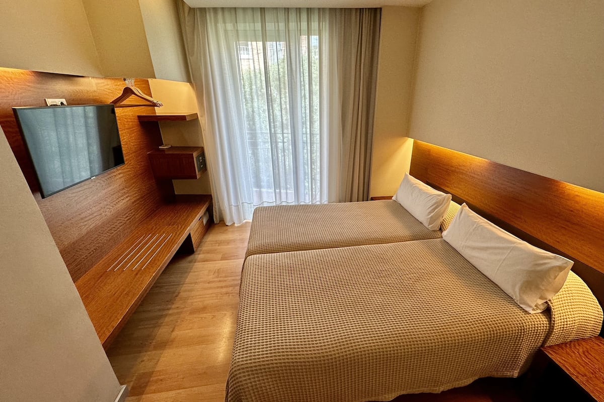 A hotel room with a bed, a TV, a desk, and a window with curtains.