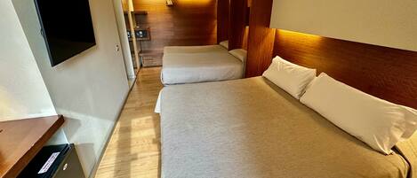 A hotel room with two beds, a small desk, a TV, and a wooden wardrobe.