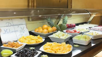 En buffet med et udvalg af frugter og snacks, blandt andet appelsiner, ananas, vandmelon og mango.