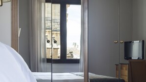 A hotel room with a bed, a television, a window with curtains, and a view of buildings outside. - Eurostars Maimónides Hotel (Córdoba)