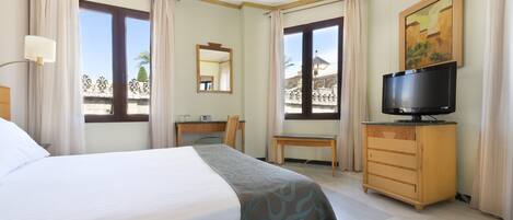 Una habitación de hotel con cama, escritorio, silla, televisor y cómoda.