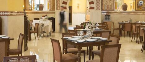 Un restaurante con varias mesas dispuestas para comer, con una decoración clásica que incluye muebles de madera y suelo de baldosas.