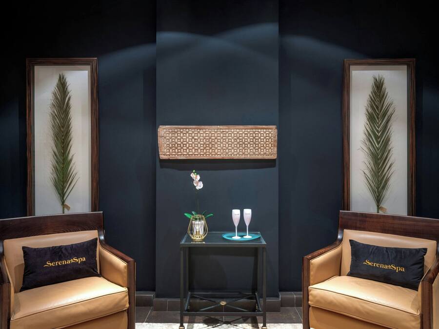 A room with two leather chairs, a small table with a vase and two glasses, framed artwork on the walls, and a dark floor.